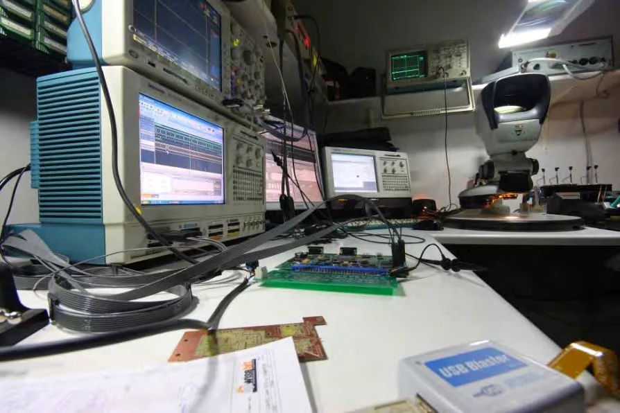 The Singularity Board under development on the lab bench, among measurement instruments and monitors